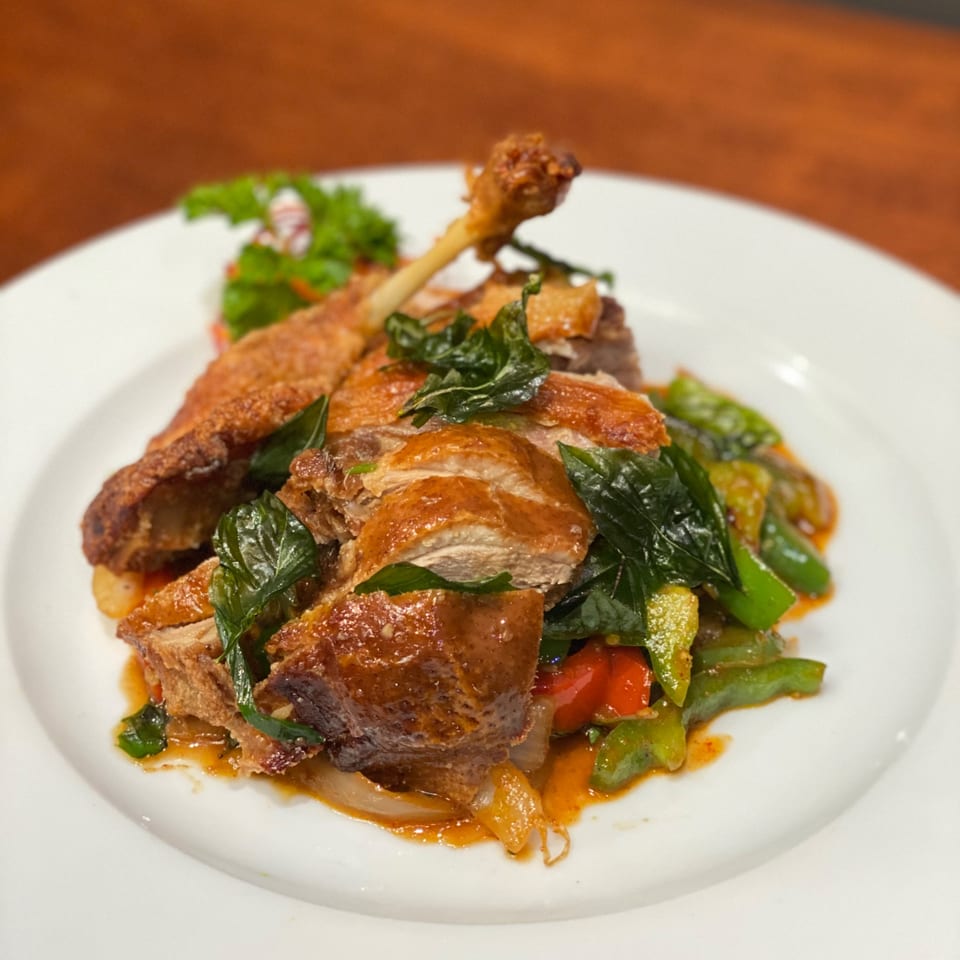 Crispy duck leg and sliced duck breast with basil, bell peppers, and onions on a white plate.