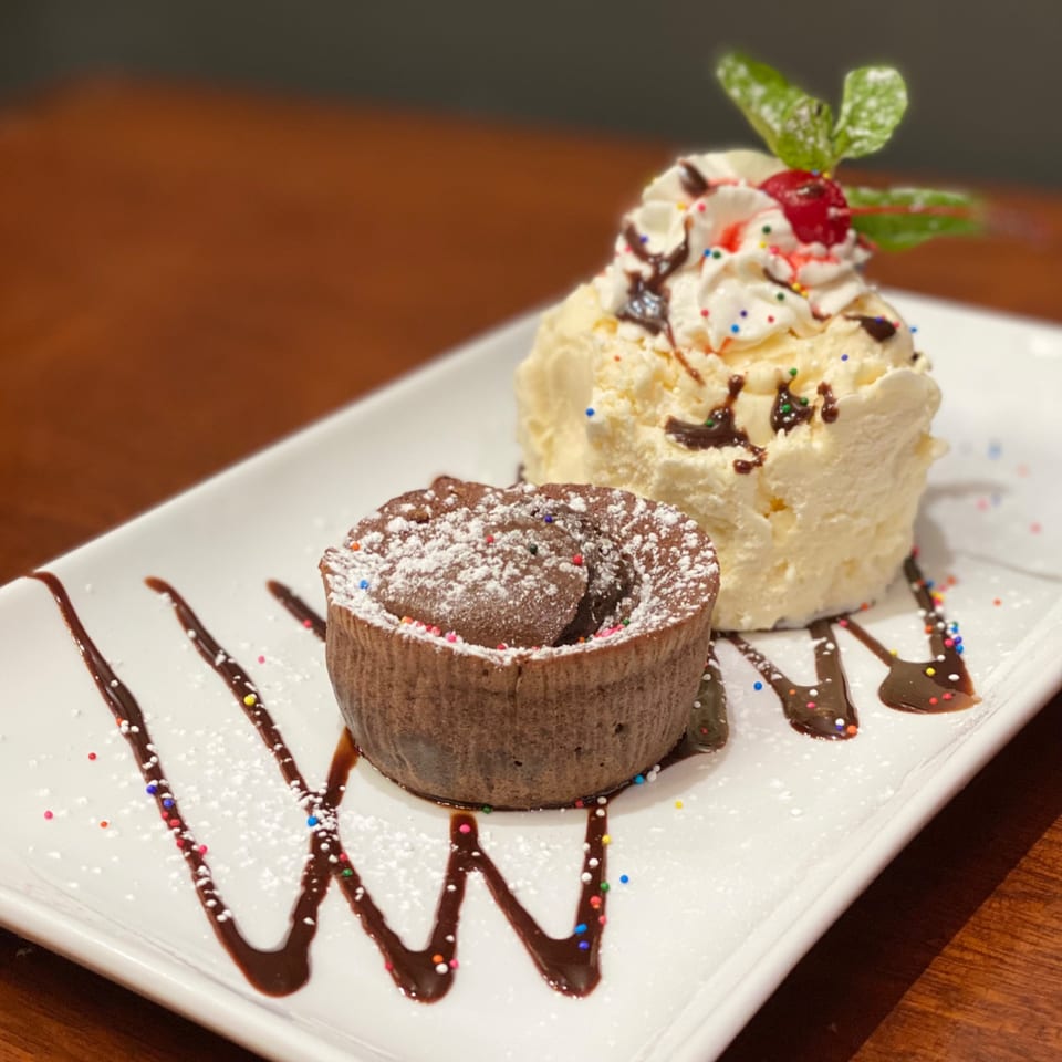 Chocolate lava cake with powdered sugar, vanilla ice cream, whipped cream, cherry, and mint.