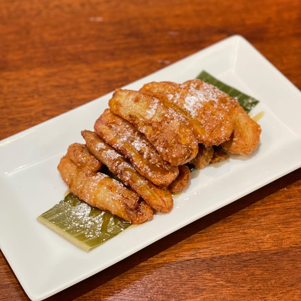 My Black Thai's fried bananas, drizzled with honey and powdered sugar, on a white plate.