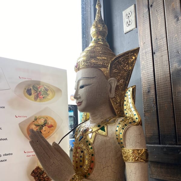 A Thai statue with gold accents and a menu displaying green and red curry dishes.
