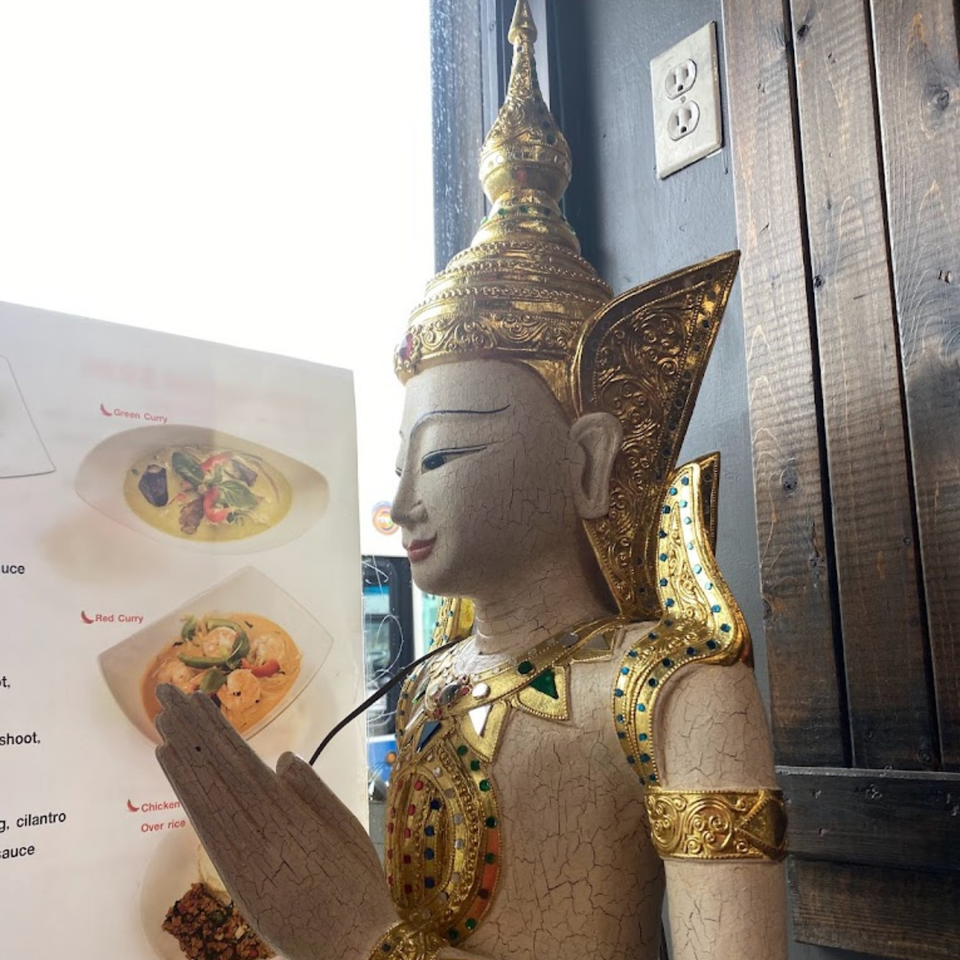 A Thai statue with gold accents and a menu displaying green and red curry dishes.