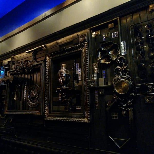 Dark, ornate wall decor with framed Buddha head, intricate carvings, and blue lighting at My Black Thai.