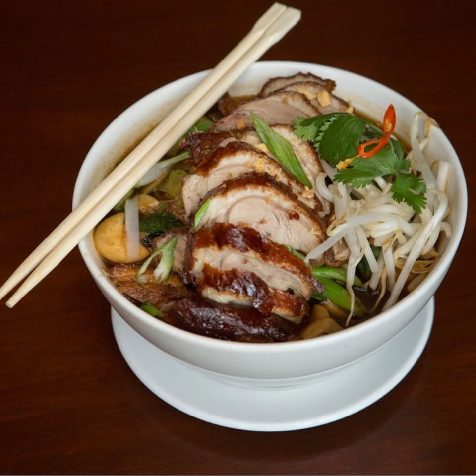 A bowl of My Black Thai duck noodle soup with chopsticks, garnished with bean sprouts and herbs.