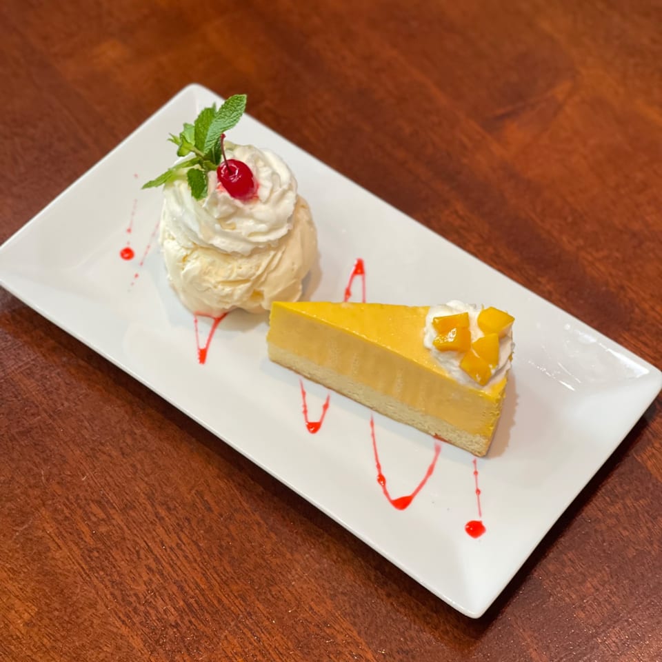 My Black Thai mango cheesecake with whipped cream, cherry, and mint, next to vanilla ice cream.