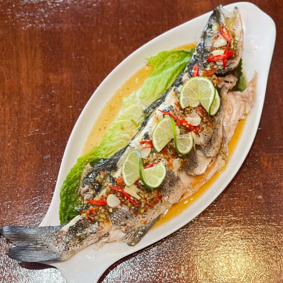 Whole steamed fish with lime slices, red chilies, and garlic on a white platter.