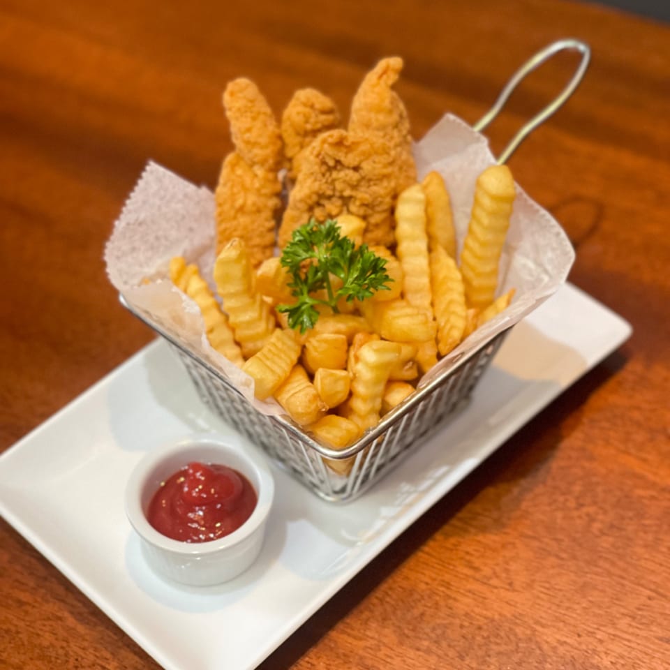Crispy chicken tenders and crinkle-cut fries in a metal basket with ketchup on a white plate.