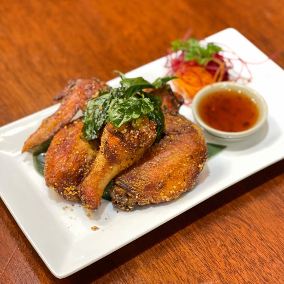 Crispy fried Thai chicken with basil, shredded vegetables, and dipping sauce on a white plate.