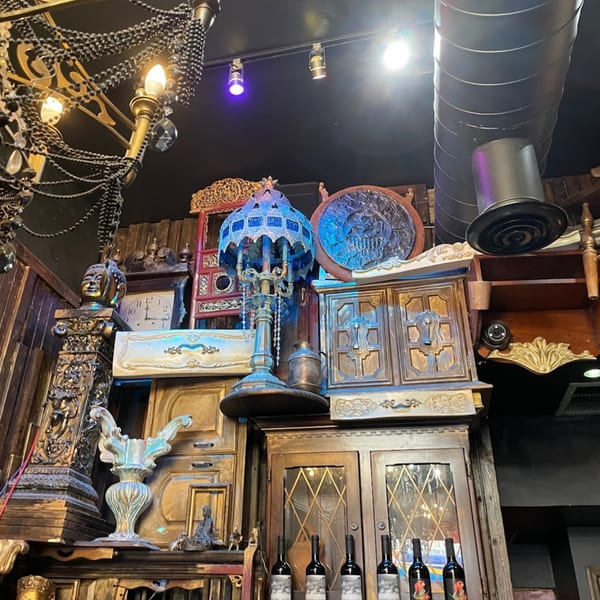 Ornate Thai decor fills the restaurant, featuring a blue lamp, golden statues, and wine bottles.