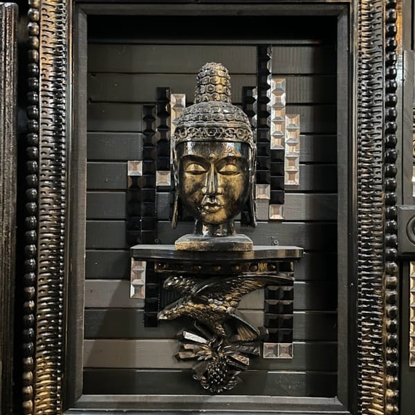 A dark, ornate Buddha head sculpture sits above a golden eagle, framed by decorative black and gold panels.